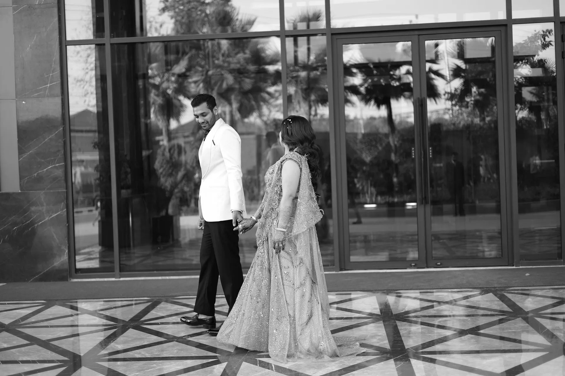 Black and white editorial photograph of a couple walking hand in hand outside a luxury hotel, by EDP Studio Lucknow